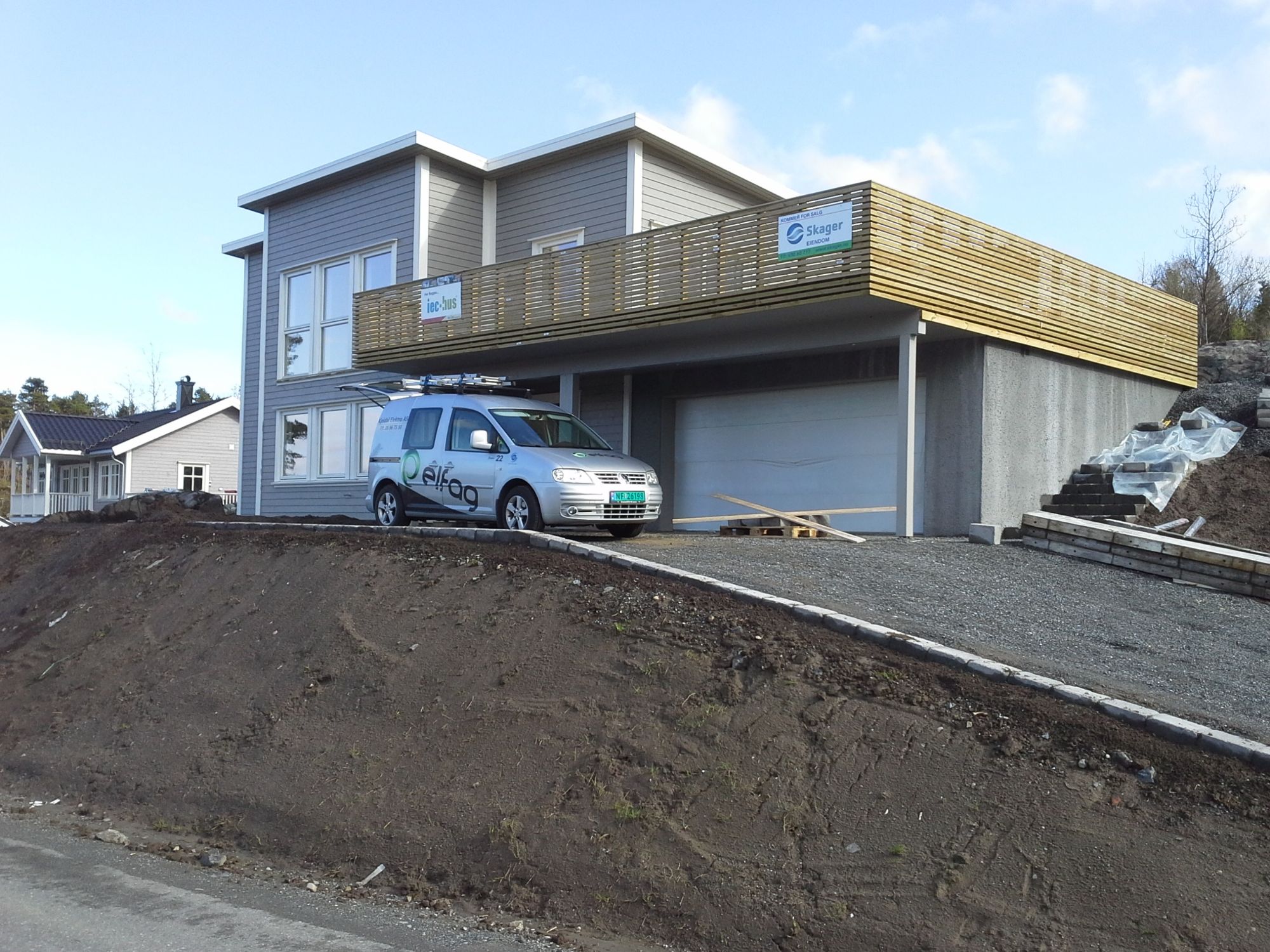 Firmabil står i innkjørselen til et moderne hus hvor en veranda holder på å bli bygd. 