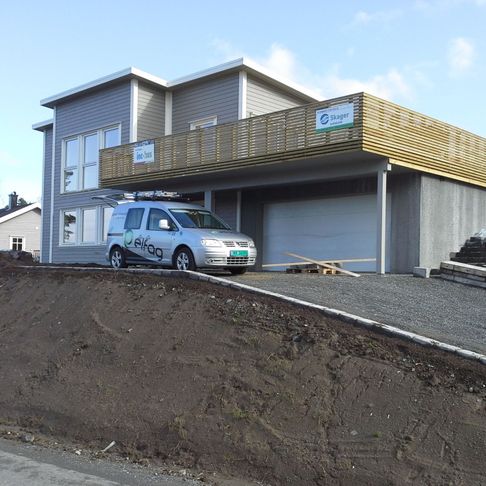 Firmabil står i innkjørselen til et moderne hus hvor en veranda holder på å bli bygd. 