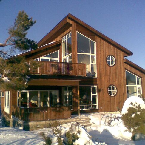 Moderne hus som står i et vinterlandskap som har skråtak og mange vindu 